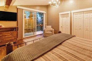 Ein Schlafzimmer mit einem großen Bett, einem Fernseher, einem Sessel und einer Glastür, die auf einen Balkon führt.
