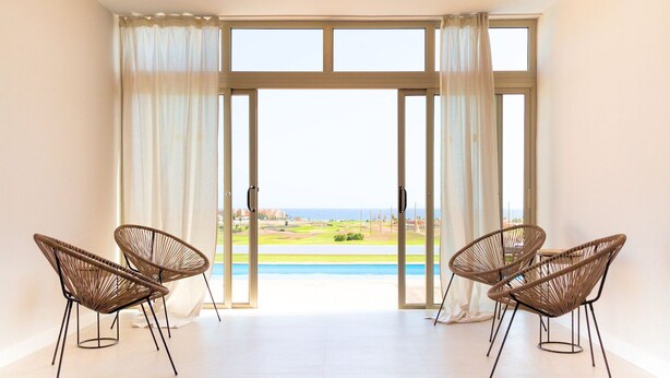 A room with two wicker chairs, a large window with curtains, and a view of a green landscape. - Villa Brisamar Azul | Caleta de Fuste | Golf Views | Heated Pool | Near Beach (Fuerteventura)