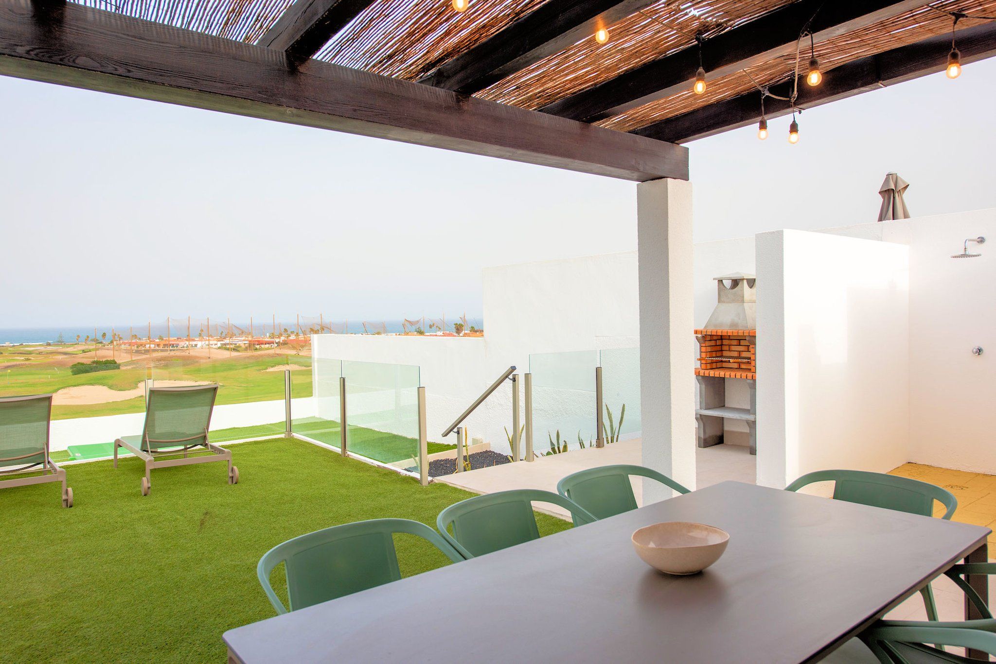 A patio with a table and chairs, a grill, and a view of a golf course.