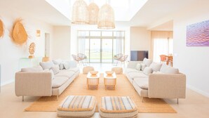 A spacious living room with a large sofa set, two round tables, and a large window with a view. - Villa Brisamar Azul | Caleta de Fuste | Golf Views | Heated Pool | Near Beach (Fuerteventura)