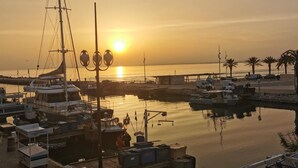 A marina with boats docked, a pier extending into the water, and a sunset in the background.