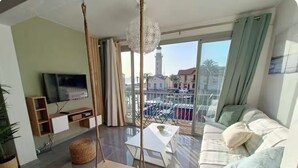 A living room with a sofa, TV, swing, and balcony with a view of buildings and a tower.