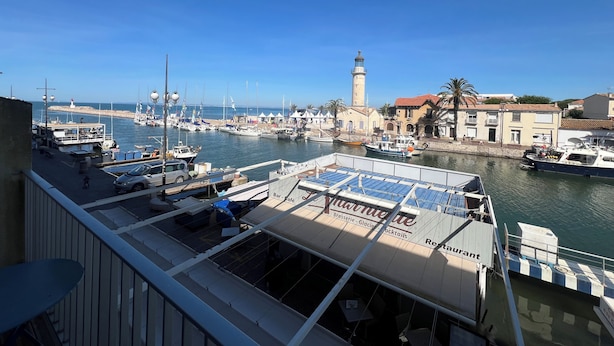 A marina with boats docked, a lighthouse, and buildings with balconies.