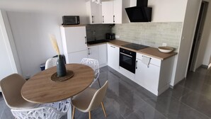 A modern kitchen with white cabinets, a black range hood, a microwave, and a sink. There is a dining table with chairs and a vase of flowers.