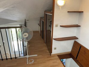 Ein Zimmer mit Holzboden, einem Standventilator, einer Treppe mit Holzwandläufen und einer Wandleuchte.