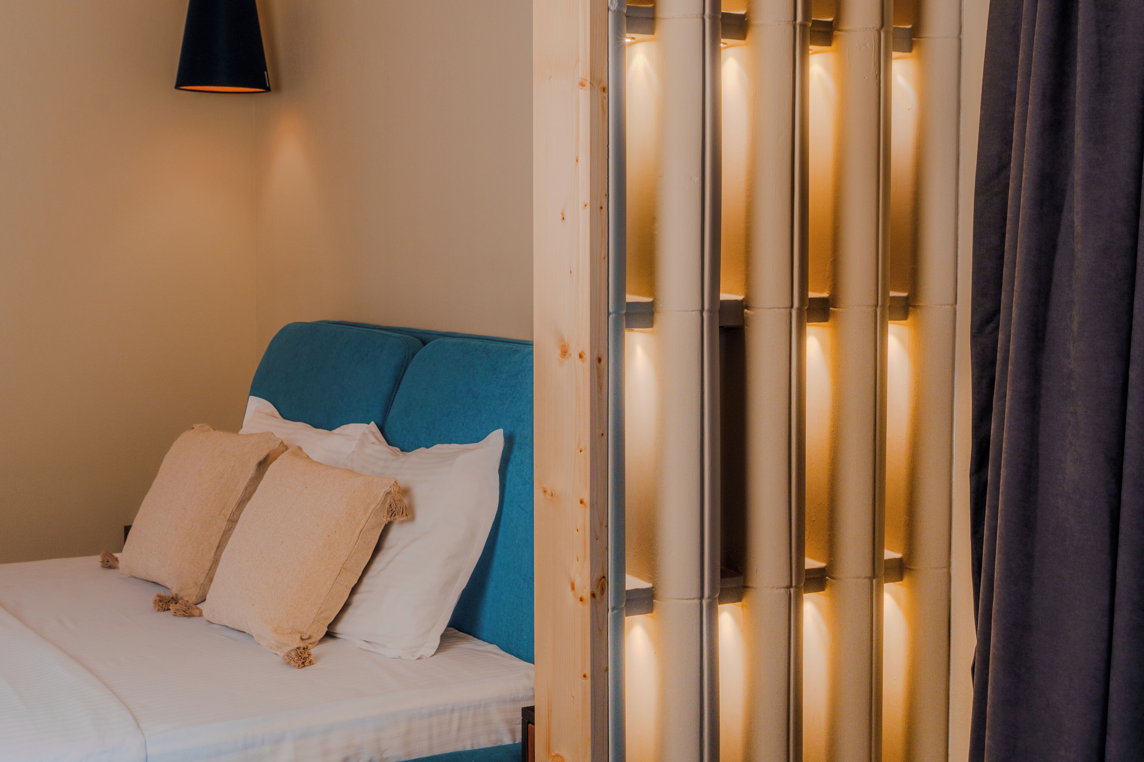 A bed with white linens and two pillows, a blue headboard, and a wall-mounted lamp.
