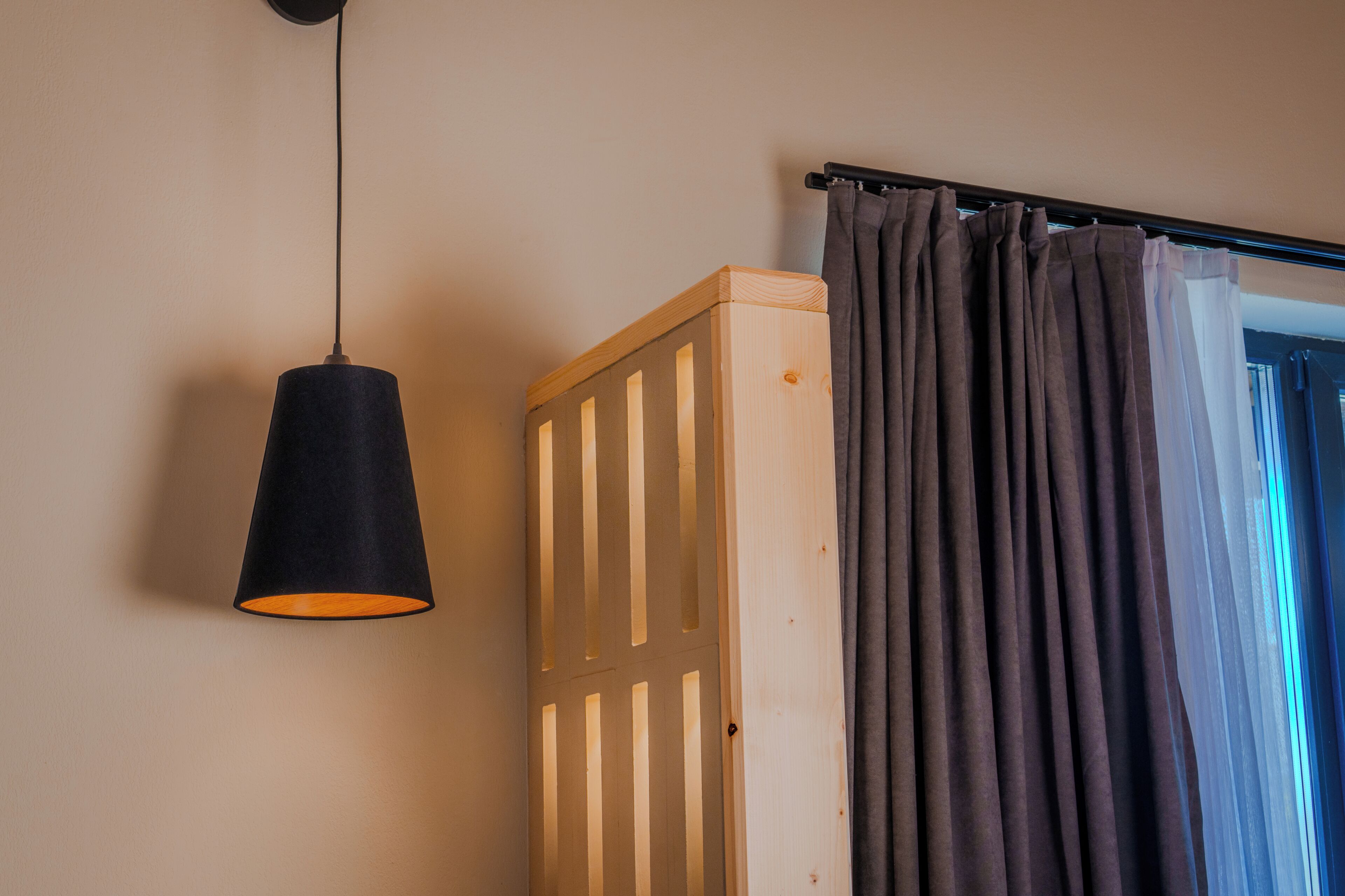 Una habitación con una cuna de madera, una lámpara colgante y una barra para cortina con cortina.