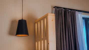 Una habitación con una cuna de madera, una lámpara colgante y una barra para cortina con cortina.