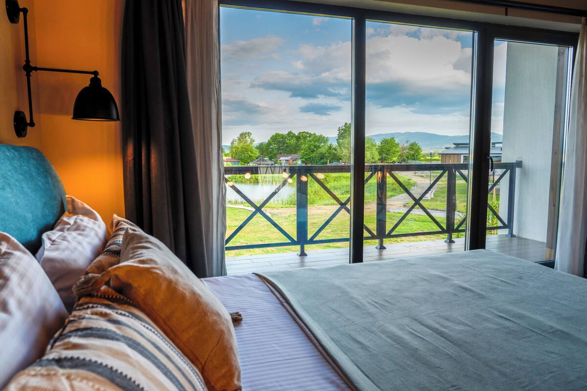 Ein Schlafzimmer mit großem Fenster, einem Bett und Blick auf einen Balkon.