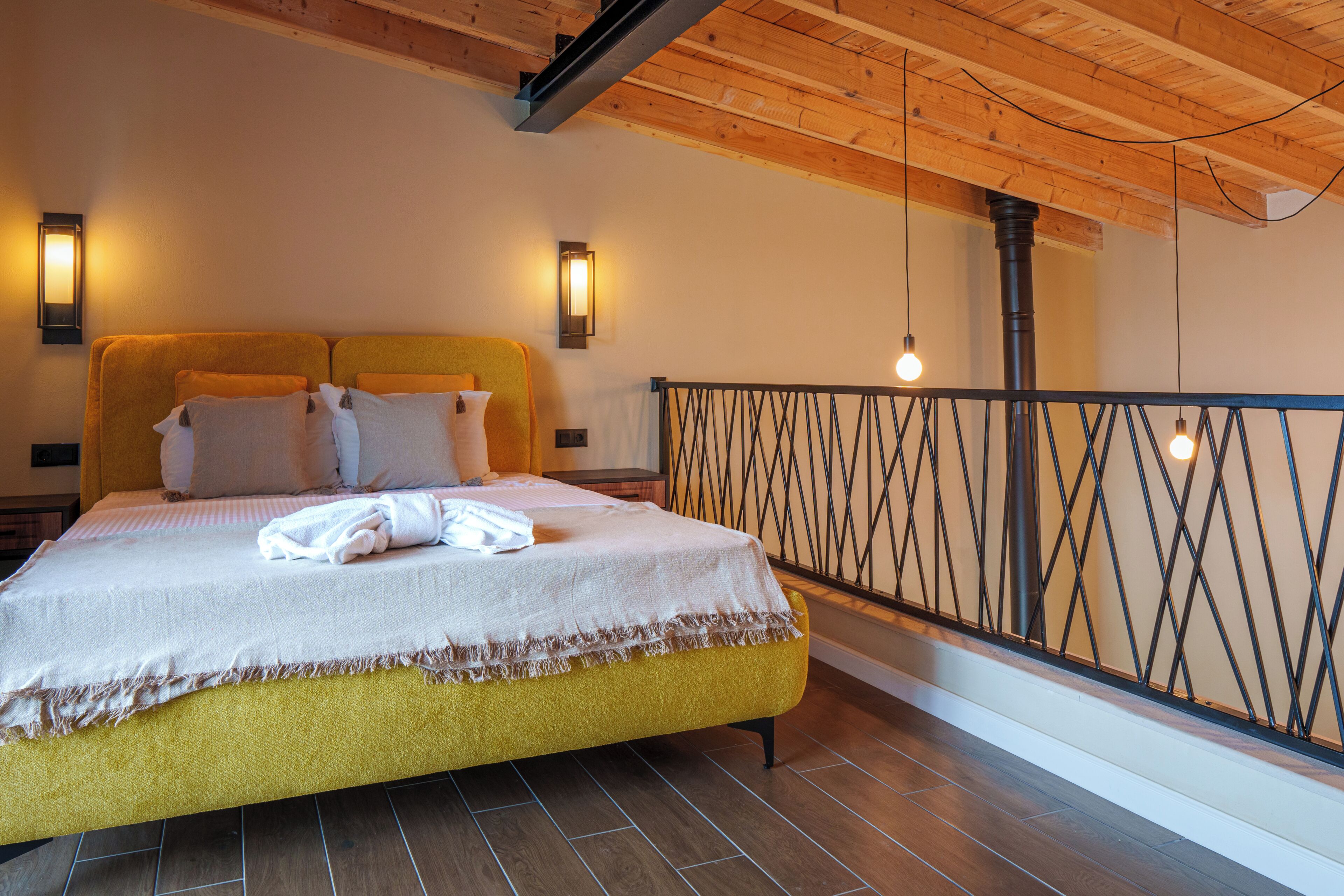 Quarto com cama, abajures, teto de madeira e guarda-corpo de varanda.