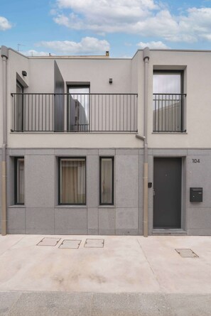 Un edificio a due piani con un balcone, una porta con la scritta '104' e una finestra con tenda.