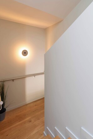 Uma escada com corrimão, um luminário na parede e um vaso de planta.