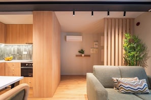 Eine moderne Küche mit Holzausstattung, einem Esstisch und einem grauen Sofa mit gemusterten Kissen.