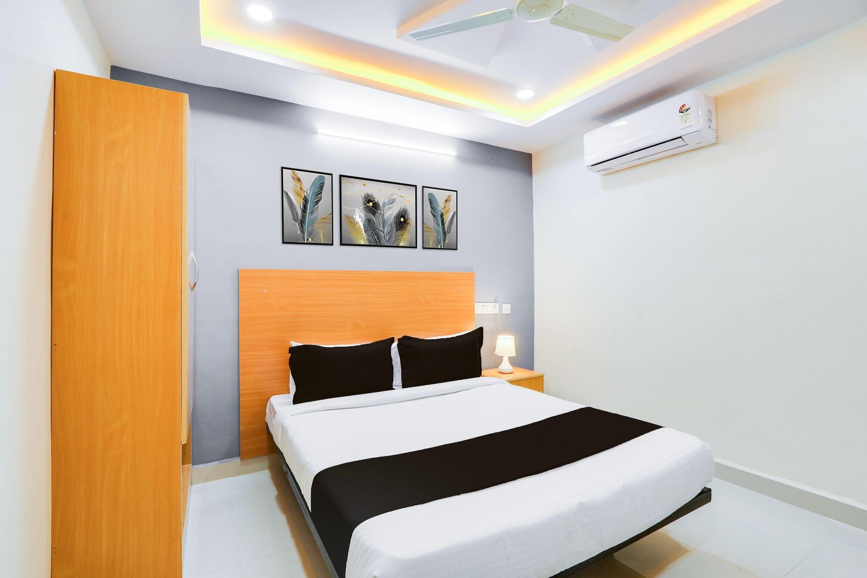 A modern hotel room with a bed, bedside table, wall-mounted air conditioner, and ceiling lights.