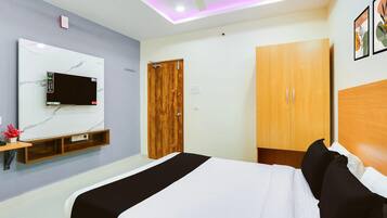 A bedroom with a bed, a TV mounted on the wall, a wooden wardrobe, and a ceiling fan.