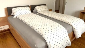 Un llit doble amb matalàs gris i roba de llit blanca amb un petit dibuix.