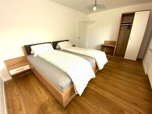 Un dormitorio con dos camas, suelo de madera, un armario y una mesita de noche.
