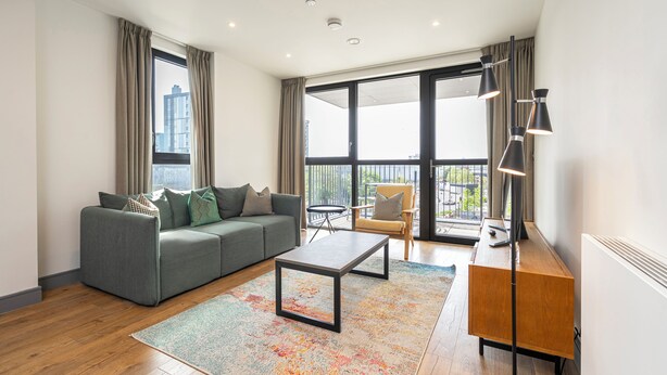 Una sala de estar moderna con un sofá gris, una mesa de centro, una mesita de noche de madera y un ventanal con cortinas.