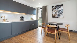 Una cocina moderna con armarios grises, una mesa de comedor de madera con sillas, y un cuadro abstracto grande en la pared.