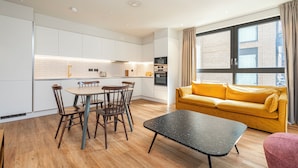 Una cocina moderna con armarios blancos, una mesa de comedor con sillas, un sofá amarillo y un ventanal con cortinas.