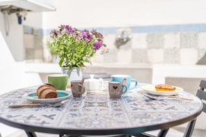 A round table with a patterned tablecloth, a vase with purple flowers, a green cup, a white teapot, a blue cup, a plate with a pastry, and two mugs with 'I love coffee' text. - Dimora Storica Laura - Salento Reservation (Alliste)
