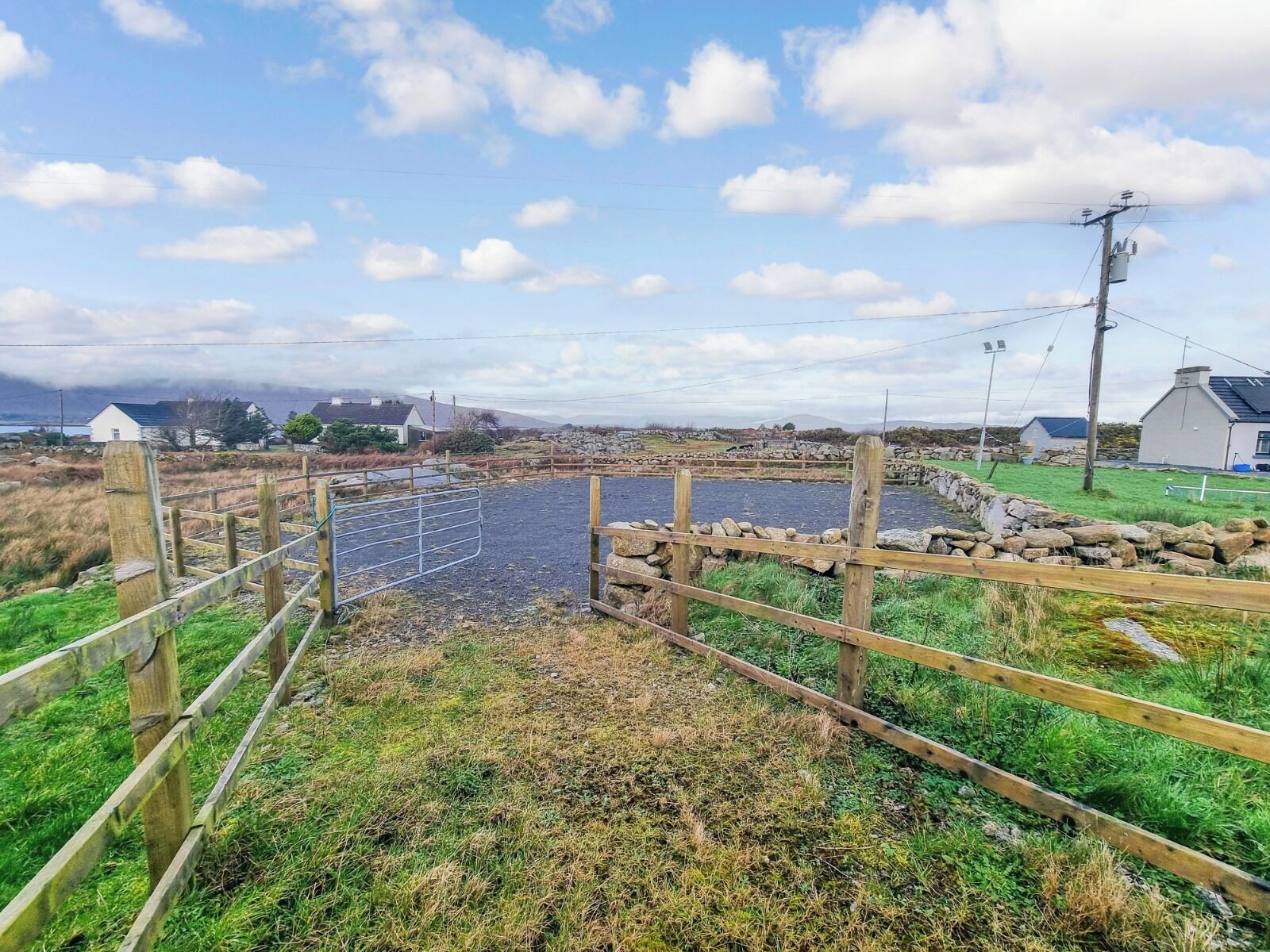 Un paysage rural avec une zone délimitée par une clôture, des murs en pierre et une étendue d’eau.