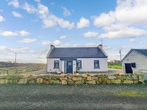 A white house with a dark roof, a stone wall in front, and a clear sky. - A little slice of heaven! (Rosmuc)