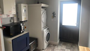 A laundry room with a washing machine, dryer, and stacked dryers. There is a control panel with a digital display and a small cabinet with a microwave. - A little slice of heaven! (Rosmuc)