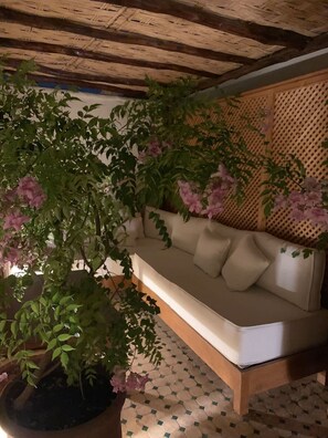 Ein Zimmer mit Holzboden, einem beigefarbenen Sofa mit Kissen und einer Pflanze mit grünen Blättern und rosa Blüten.