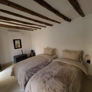 Ein Schlafzimmer mit zwei Betten, Holzbalken an der Decke, einem kleinen Nachttisch mit einer Vase und einer Wandleuchte.
