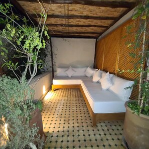 A cozy outdoor sleeping area with a cushioned bench and a wooden frame, surrounded by greenery and a patterned floor. - Petit Pacha Your Ultimate Escape Awaits you (Marrakech)