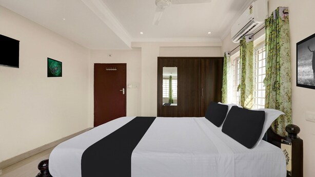 A hotel room with a bed, a ceiling fan, an air conditioning unit, a door, and a window with curtains. - Classic With Balcony The Best Inn (Kakinada)