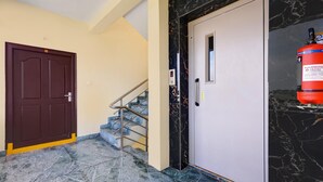 A marble-floored hallway with a brown door, a staircase, and a fire extinguisher mounted on the wall. - Classic With Balcony The Best Inn (Kakinada)