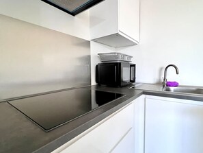 Eine moderne Küche mit einem schwarzen Induktionskochfeld, einer Mikrowelle und einem Edelstahl-Spülbecken.