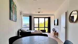Une chambre moderne avec une table ronde, un canapé, un téléviseur et une grande fenêtre donnant sur la ville.