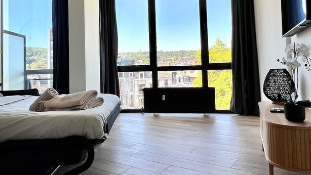 Une chambre d’hôtel avec un lit, de grandes fenêtres, un ventilateur de plafond et un téléviseur fixé au mur.