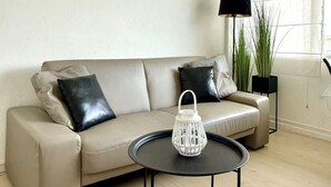 A living room with a sofa, a round coffee table, a floor lamp, and a potted plant. - Small Cozy Nest for 4 People 100 m From the Beach Free Parking (De Haan)