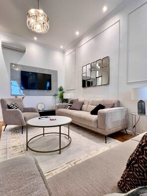 Un salon moderne comprenant un canapé, un fauteuil, une table basse, un téléviseur et des miroirs décoratifs.