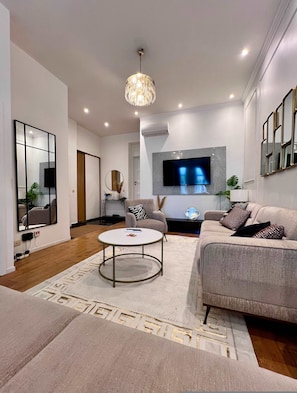 A modern living room with a round coffee table, a sofa, a TV, and a chandelier. - Cozy Apartment for 9 Guests Brussels Midi Station (Brussels)