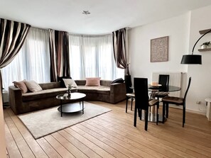 A modern living room with a sectional sofa, a round coffee table, and a dining area with chairs and a table. - Sablon Centre Cozy Apartment Near the Museums (Brussels)
