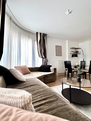 A modern living room with a sofa, a coffee table, and a dining area with chairs and a lamp. - Sablon Centre Cozy Apartment Near the Museums (Brussels)