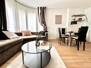 A modern living room with a glass coffee table, a sofa, and a dining area with chairs and a table. - Sablon Centre Cozy Apartment Near the Museums (Brussels)