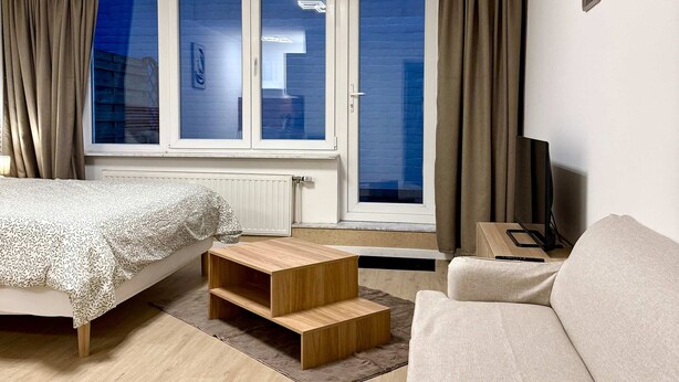 Ein modernes Schlafzimmer mit Bett, Sofa, Fernseher und einem Fenster mit Vorhängen.
