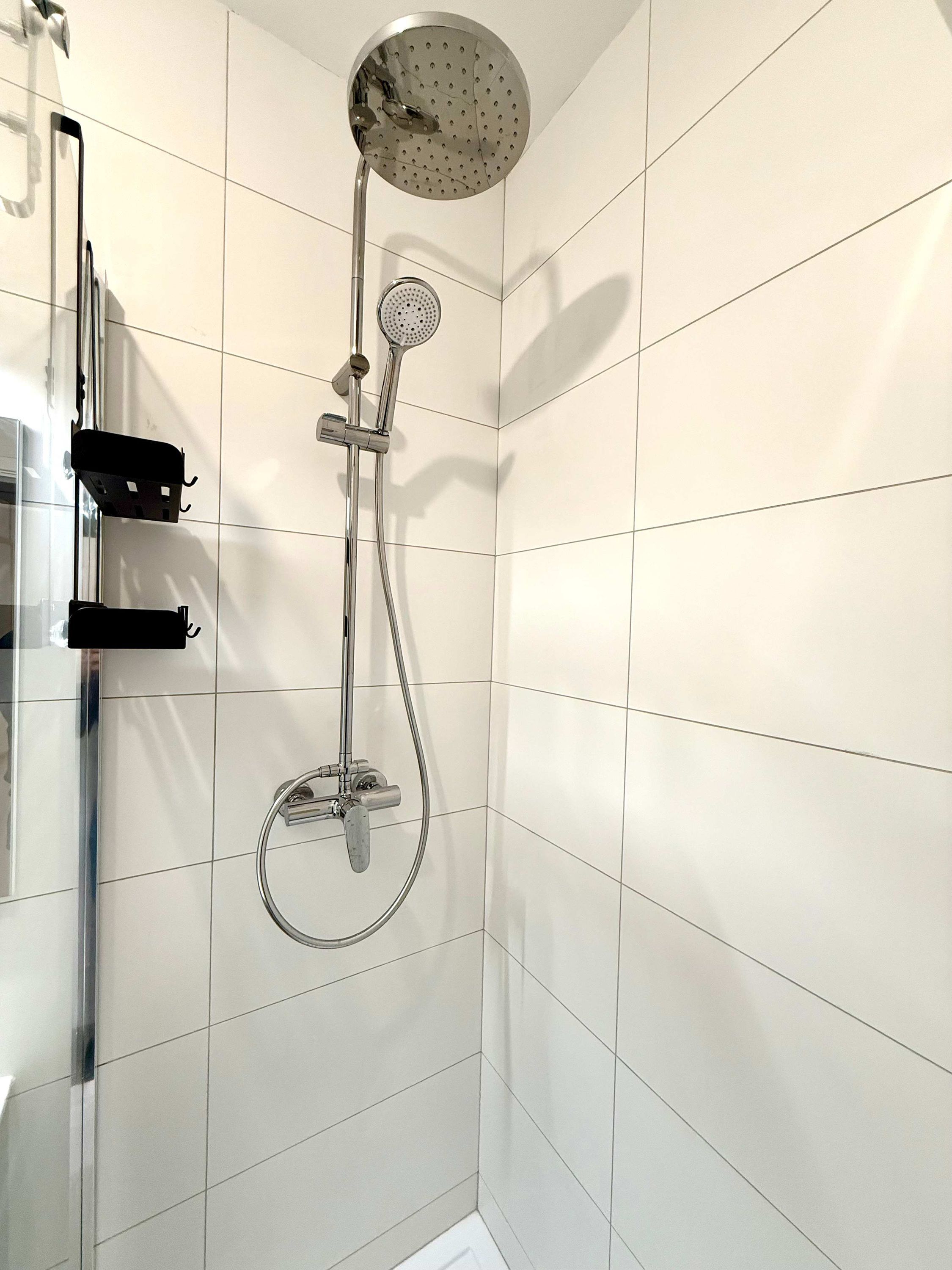 A modern shower with a handheld showerhead, a fixed showerhead, and a handheld shower hose.