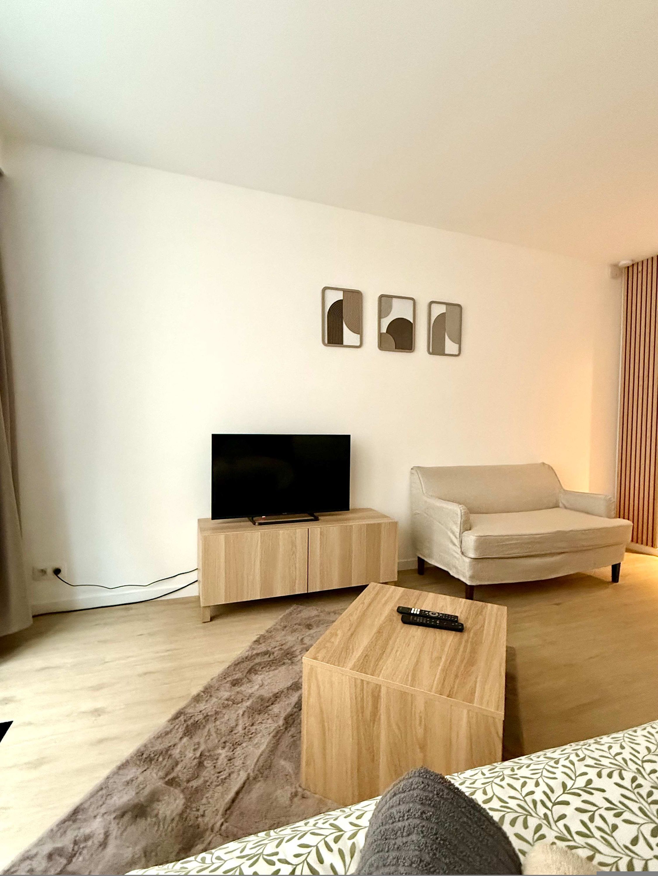 Un salon avec un téléviseur posé sur un meuble en bois, un canapé, une table basse et trois tableaux encadrés accrochés au mur.
