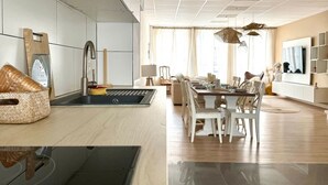 A modern kitchen with a built-in stove, a dining area with a table and chairs, and a large window providing natural light. - Spacious Duplex in the Center of Bastogne Onikos Rooms (Bastogne)
