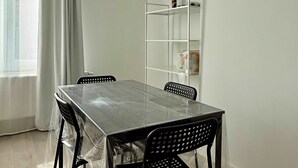 A dining area with a table, chairs, a shelf with items, and a window with curtains. - Doux nid Perche Avec vue Magique sur la Ville (Brussels)