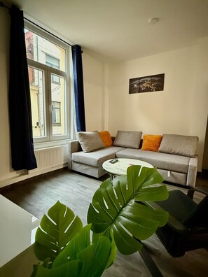 A modern living room with a grey sofa, a white coffee table, and a large green plant. - Gare du Midi for 3-4 People (Brussels)