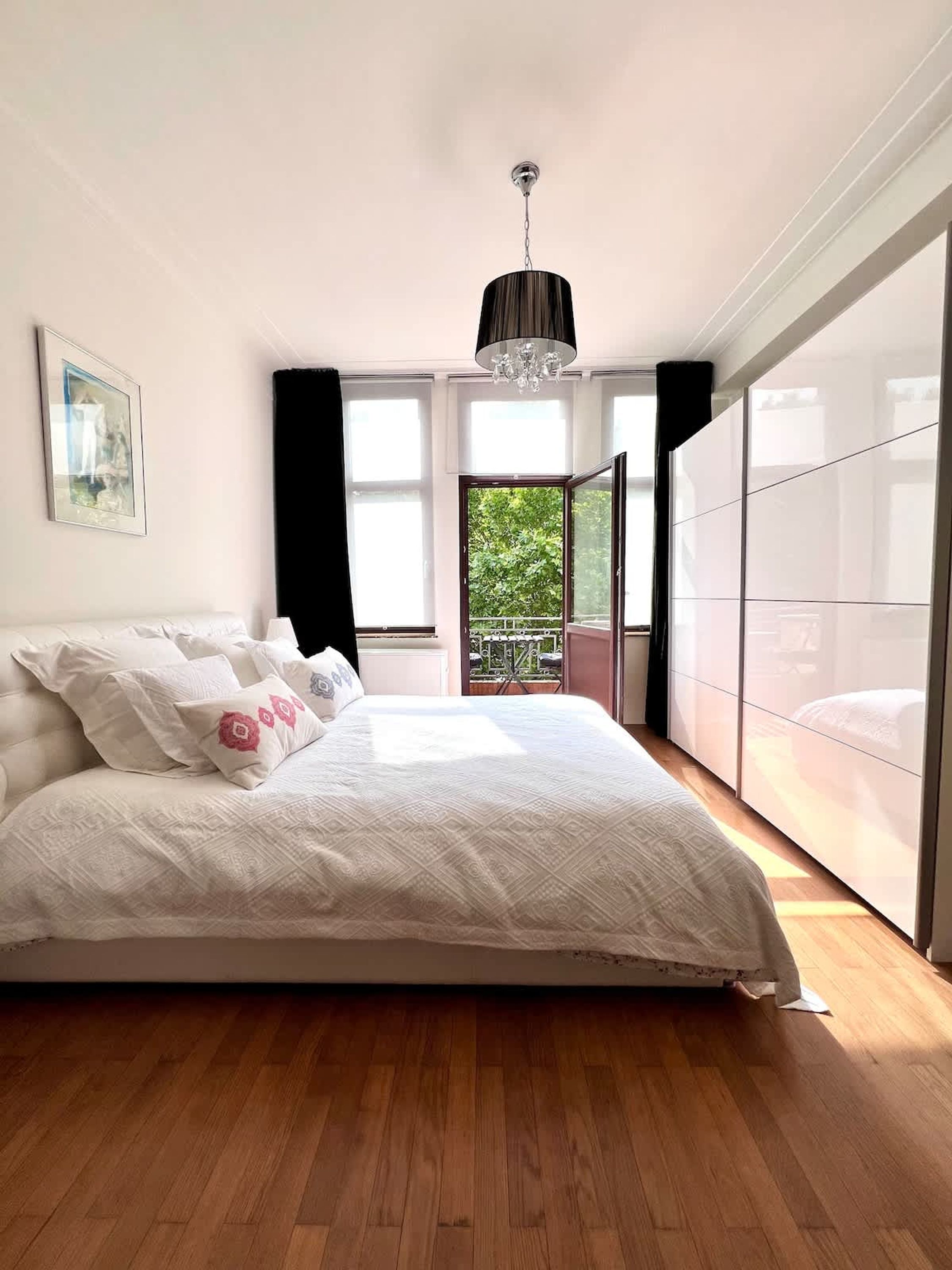 Quarto com uma cama grande, um candelabro, uma janela com vista para o verde e uma porta de correr de vidro.