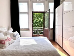 A bedroom with a bed, a wardrobe, and a balcony with a view of greenery. - A Chic Haven in the Heart of Urban Nature (Brussels)